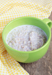 Green buckwheat porridge with milk on wooden table