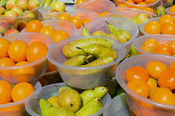 Bowls of oranges, pears, satsumas and apples for sale on a sunny day at a market stall in East London.