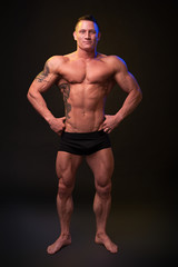 Fototapeta na wymiar Beautiful physique bodybuilder on a dark background