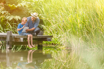 father and son using a tablet on a wooden pontoon in summertime
