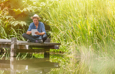 handsome man sitting on a wooden pontoon and using a digital tab