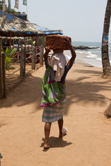 The Indian woman in a sari stones for building on the head on a beach. India Goa