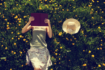 Girl lying in grass, reading a book. - obrazy, fototapety, plakaty