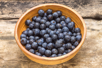 Ripe blackthorn berries in clay bowl on wood background