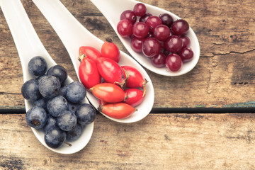 Fresh wild berries in ceramic spoons on wood background.