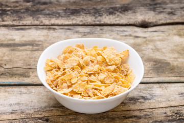 Corn flakes in white bowl on wood background