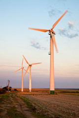 Wind turbine at sunset on green field.