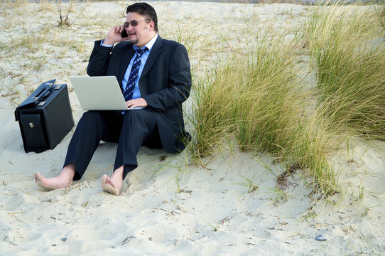 Geschäftsmann sitzt am Sandstrand und arbeitet am Computer