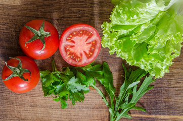 Juicy tomatoes with green-stuff on wooden table