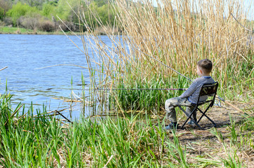 Fototapeta na wymiar Young Boy Sitting on Chair and Holding Fishing Rod