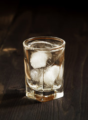 Clold fresh water with ice in a glass on a dark background in vi