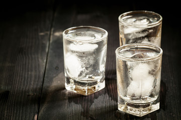 Clold fresh water with ice in a glass on a dark background in vi