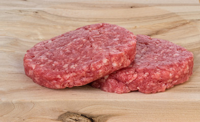 two fresh raw hamburgers over wood board