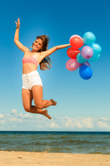 Girl jumping with colorful balloons on beach