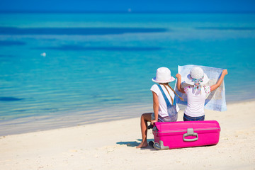 Little girls with big suitcase and map at tropical beach