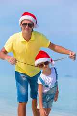 Obraz premium Little girl and happy dad in Santa Hat during beach vacation