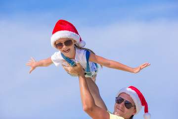 Obraz premium Little girl and happy dad in Santa Hat during beach vacation