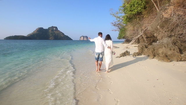 bride and groom walk barefoot along edge of water by cliffs	