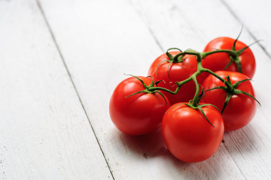 Tomatoes on branch with white wooden background