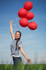 Happy young woman with a red balloon on a green meadow