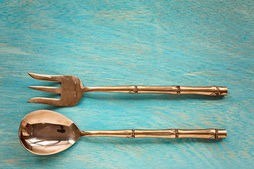 Serving brass spoon and fork on blue wooden background, top view