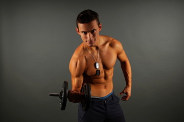 Young man exercises with dumbbell on the gray background