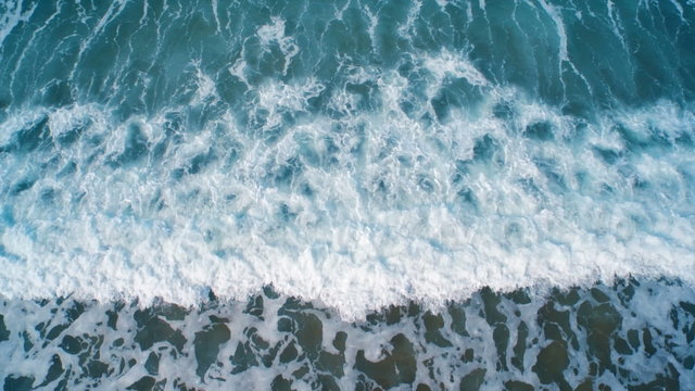 Aerial drone video of sea waves breaking on shore. Zoom out shot of ocean waves creating a texture from the white sea foam. Overhead perspective. HD 1080 video.
