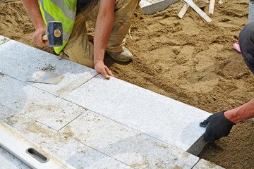 Worker tapping paver into place with rubber mallet.