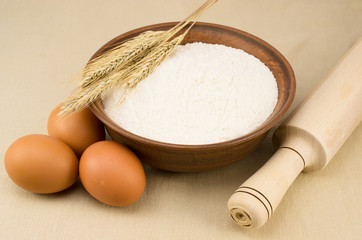 flour, egg, clay plate with flour and wheat ear on the tableclot