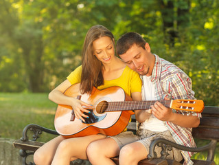 Young couple in love playing acoustic guitar in the park
