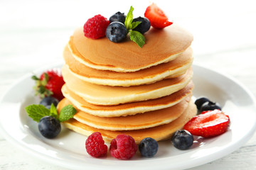 Delicious pancakes with berries on white wooden background