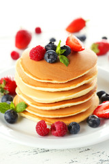 Delicious pancakes with berries on white wooden background