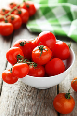 Fresh cherry tomatoes in bowl on grey wooden background