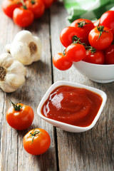  cherry tomatoes with bowl of ketchup on wooden background