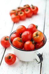 Fresh cherry tomatoes in cup on white wooden background