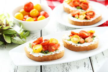 Tasty fresh bruschetta with tomatoes on plate on white wooden ba