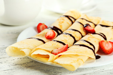 Rolled pancakes with strawberry on plate on wooden background