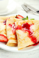 Pancakes with strawberry on plate on white wooden backgound