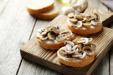 Tasty fresh bruschetta with mushrooms on cutting board on grey w