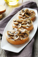 Tasty fresh bruschetta with mushrooms on plate on grey wooden ba