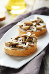 Tasty fresh bruschetta with mushrooms on plate on grey wooden ba