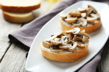 Obraz na płótnie Canvas Tasty fresh bruschetta with mushrooms on plate on grey wooden ba