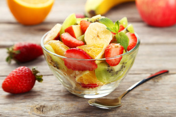 Fresh fruit salad in bowl on grey wooden background