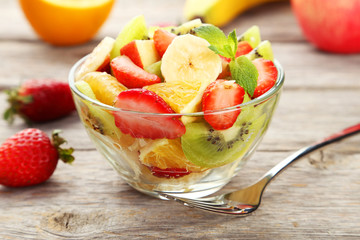 Fresh fruit salad in bowl on grey wooden background