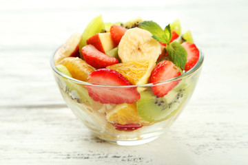 Fresh fruit salad in bowl on white wooden background