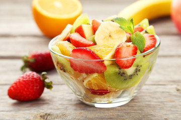 Fresh fruit salad in bowl on grey wooden background
