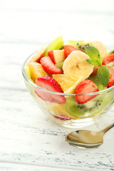 Fresh fruit salad in bowl on white wooden background
