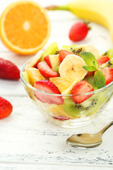 Fresh fruit salad in bowl on white wooden background