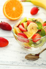 Fresh fruit salad in bowl on white wooden background