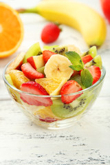 Fresh fruit salad in bowl on white wooden background